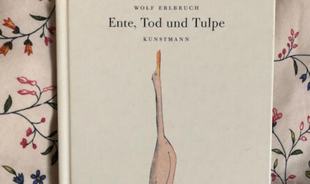 Das Bilderbuch "Ente, Tod und Tulpe" von Wolf Erlbruch liegt auf einem geblümten Kissen. Auf dem Cover des Buches ist die Ente zu sehen, die nach oben schaut (sie sieht aus wie ein Gans: weiß und langer Hals).