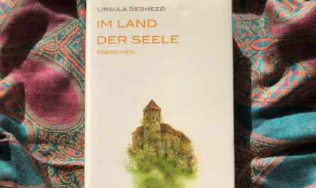 Das Buch "Im Land der Seele" von Ursula Seghezzi liegt auf einem bunten Schal. Auf dem Cover ist eine mit Blumen bewachsene Burg abgebildet.
