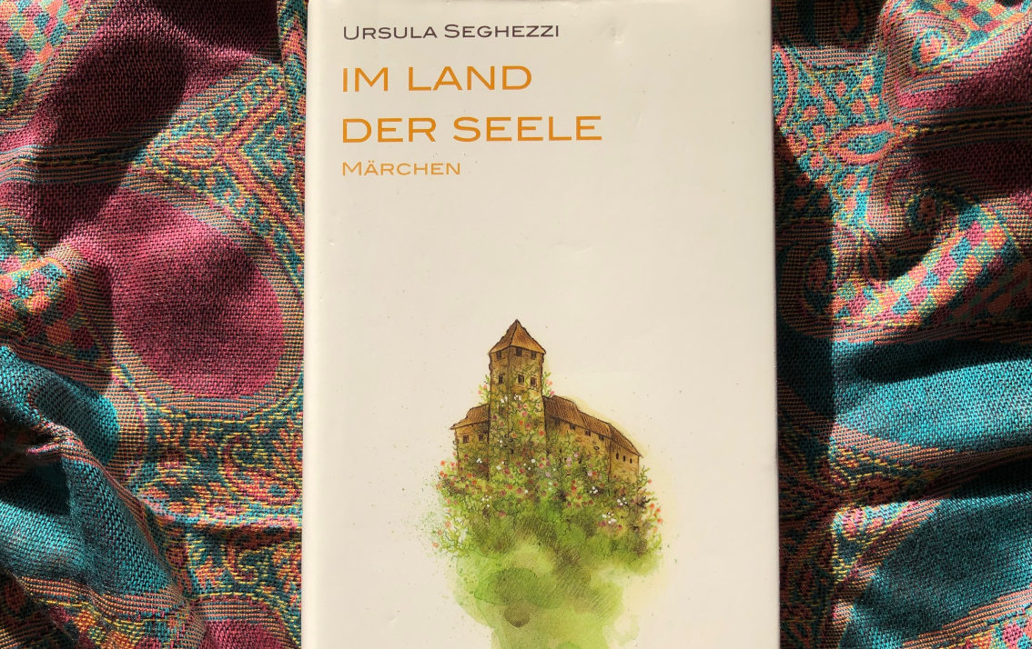 Das Buch "Im Land der Seele" von Ursula Segghezzi. Auf dem Cover steht unter dem Titel "Märchen", darunter ist eine mittelalterliche Burg auf grüner Wiese, umrankt von Blumen, abgebildet, vermutlich ein Aquarell.